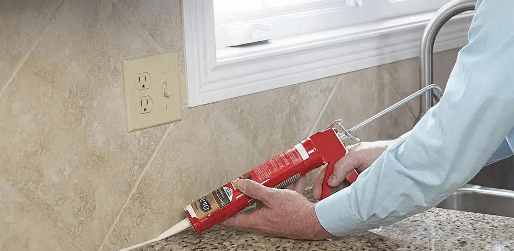 Handyman applying caulk along a kitchen backsplash and countertop seam in Atlanta, GA