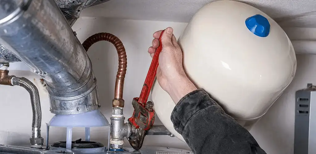 Water heater repair technician tightening plumbing connections near a tank unit in Atlanta, GA